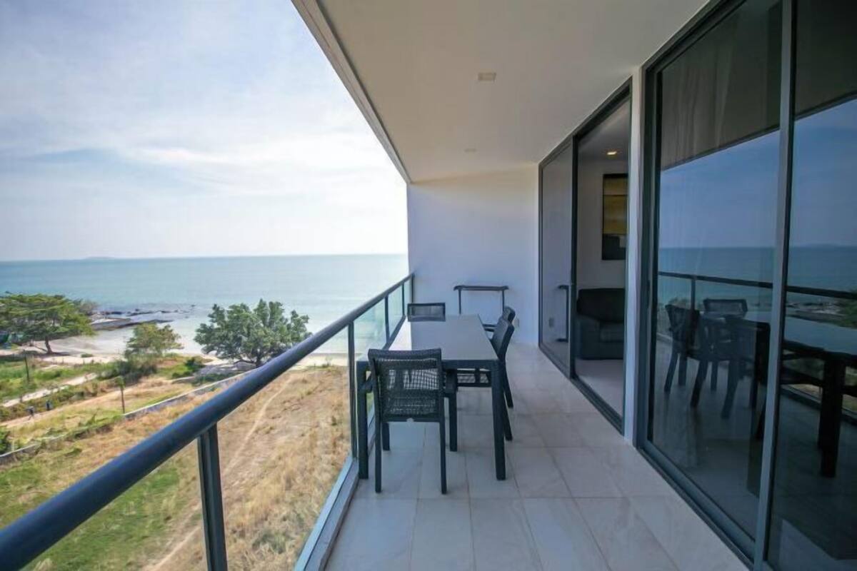 A balcony with a table and chairs, overlooking a body of water and greenery.