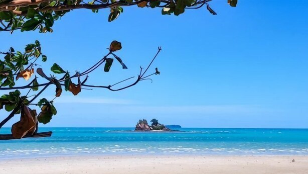 Une plage à l’eau d’un bleu limpide, avec un rivage sablonneux et une île qui se profile à l’horizon.