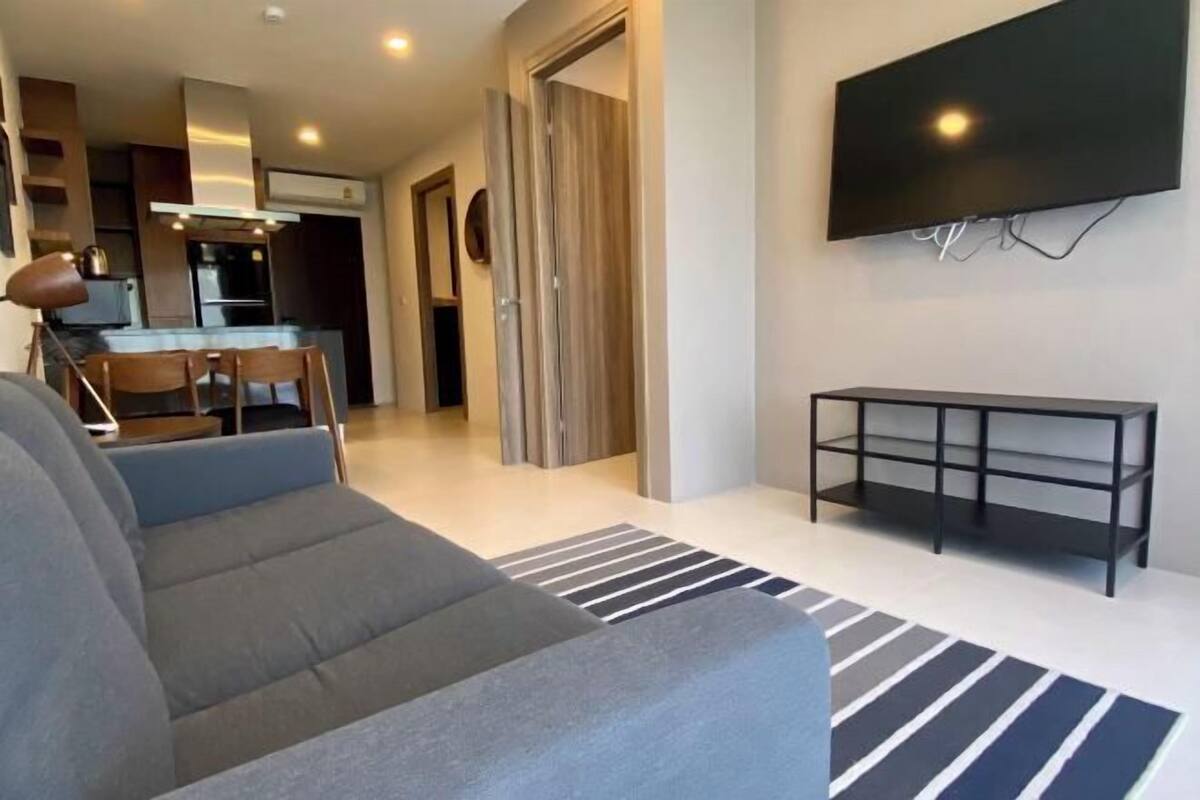 A modern living room with a sofa, a TV, and a dining area with chairs and a table.