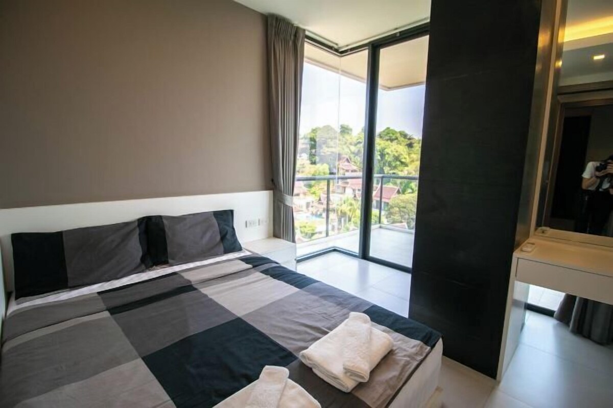 A modern hotel room with a large bed, a balcony with a view, and a large mirror.