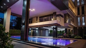 Un immeuble moderne à plusieurs étages, doté d’une piscine, de balcons et d’une façade bien éclairée.