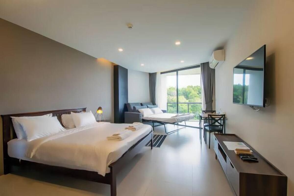 A modern hotel room with a large bed, a desk, a chair, and a TV mounted on the wall.