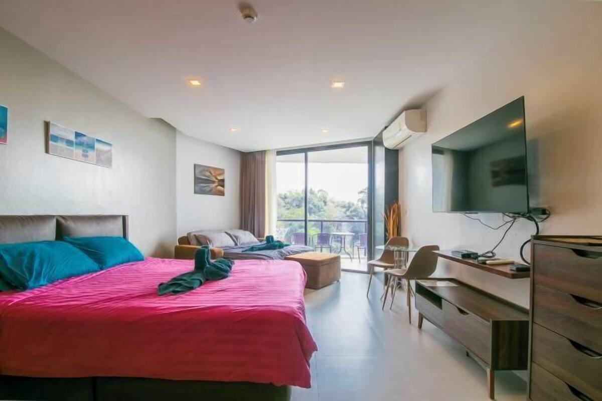 A hotel room with a bed, a desk, a chair, a TV, and a balcony with a view.