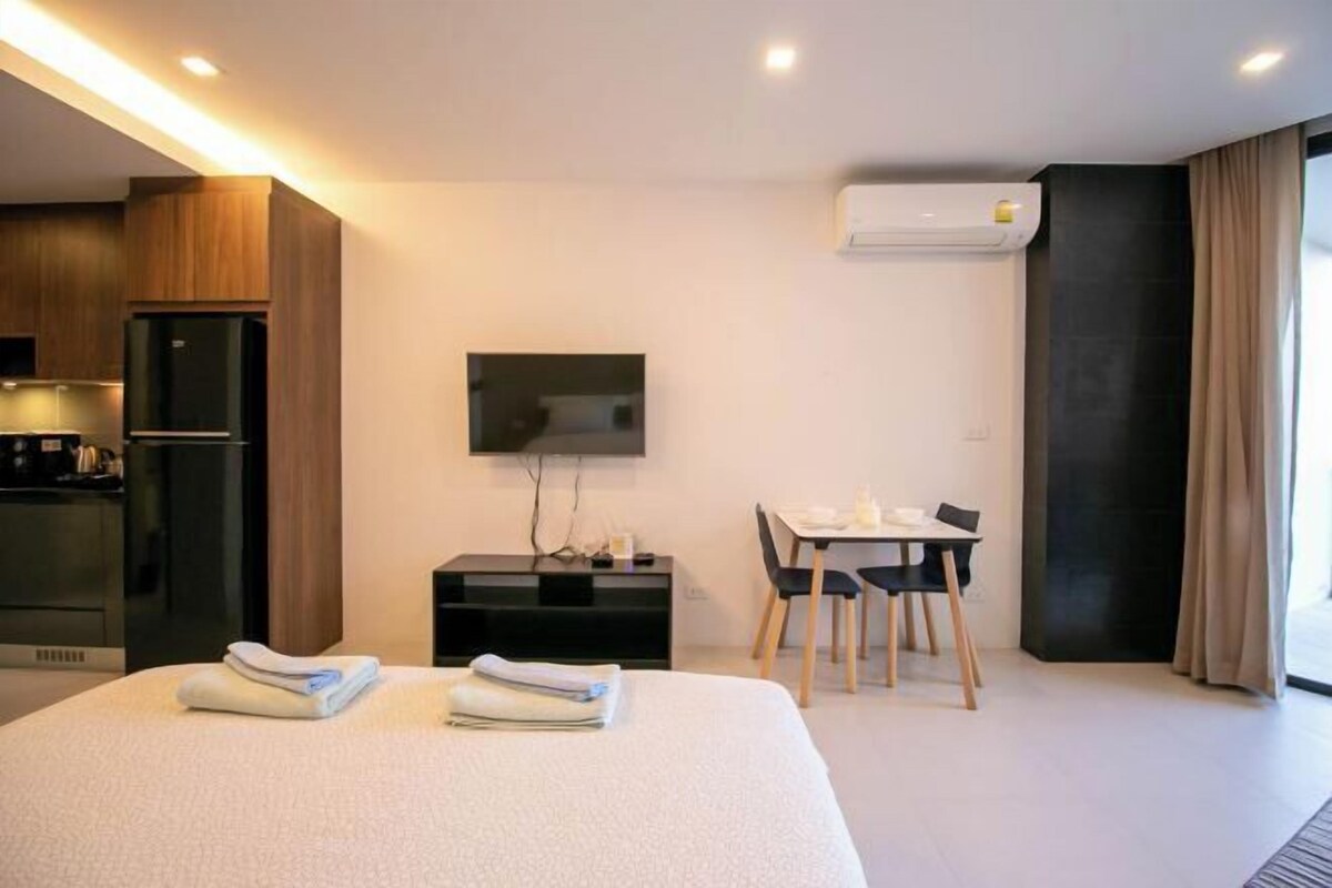 A modern hotel room with a bed, a desk, a flat-screen TV, a wardrobe, and a built-in air conditioning unit.