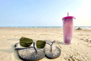 Flip-flops and a tumbler on a sandy beach.