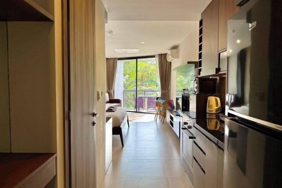 A modern kitchen with a refrigerator, microwave, and stove, leading to a balcony with a view of greenery.