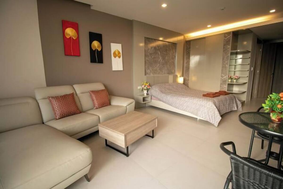 A modern hotel room with a sofa, a bed, a coffee table, and a dining area.