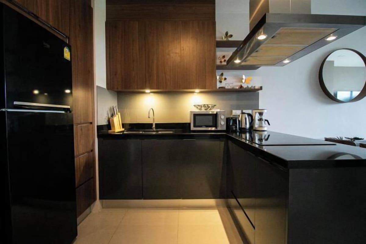 Una cocina moderna con armarios oscuros, un refrigerador negro, un microondas y una cafetera.