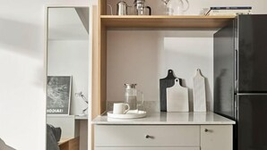 Una cuina moderna amb un frigorífic negre, armaris blancs i una cafetera a la superfície.