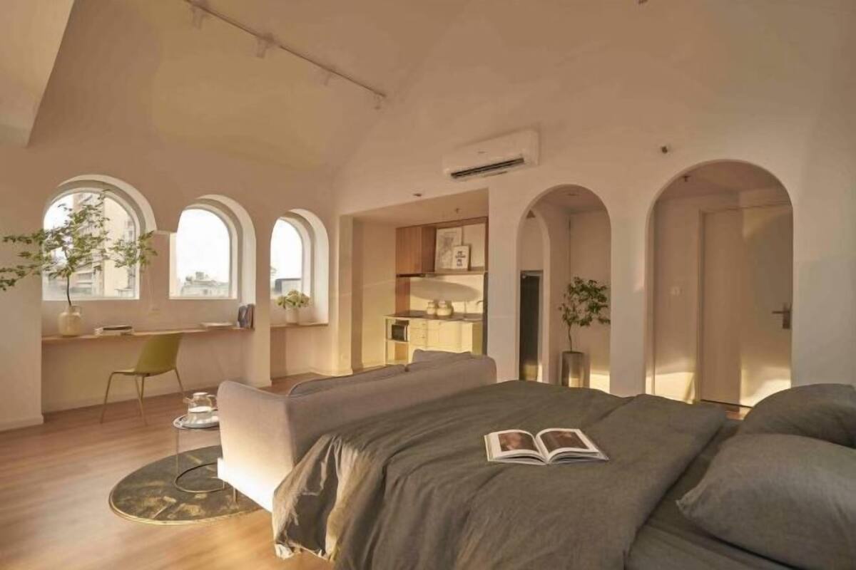 Un dormitorio moderno con una cama grande, un escritorio y una silla. Se observan puertas en arco y vistas de la ciudad.