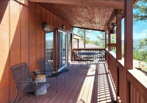 Een houten terras met buitenmeubilair, een glazen deur naar binnen en uitzicht op het omliggende landschap.