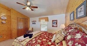 A bedroom with wooden walls, a bed with floral bedding, a ceiling fan, and a window with blinds. - 3-bedroom house in welcoming Ruidoso with AC (Ruidoso)