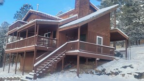 Uma cabana de madeira com varanda e escadas, rodeada por árvores cobertas de neve.
