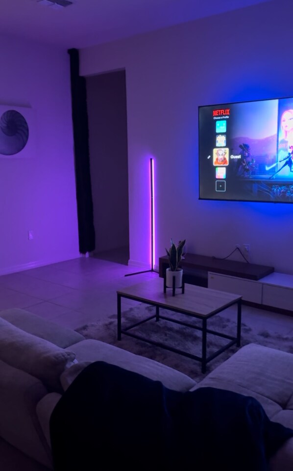 A modern living room with a flat-screen TV mounted on the wall, a sofa, a coffee table, and a potted plant. - Modern Villa (Haines City)