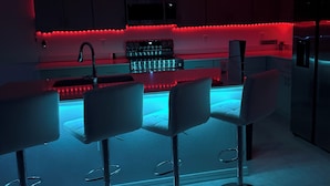 Una cocina moderna con una isla central, taburetes de bar e iluminación roja debajo de los armarios.