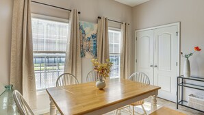 A dining area with a wooden table, white chairs, a vase with flowers, and a view of the outside through large windows with curtains. - < 4 Mi to UAB & Dtwn: Updated Birmingham Apt (Birmingham)