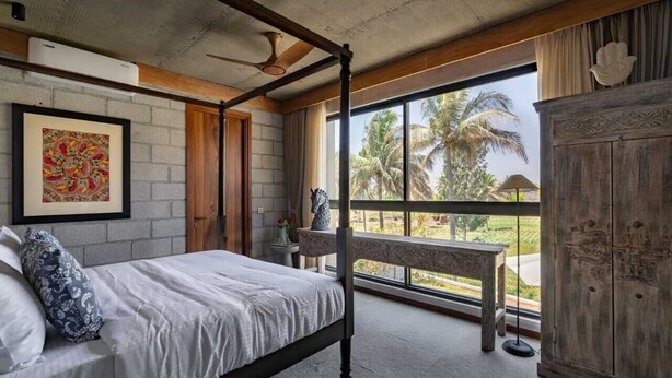 Ein Schlafzimmer mit Himmelbett, großem Fenster und Blick auf Palmen, einer Holzbank und einem Schrank.