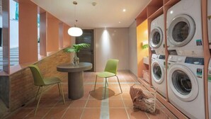 Une buanderie équipée de plusieurs machines à laver, une table avec des chaises et une plante en pot.