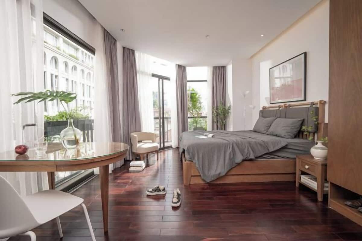 A modern bedroom with a bed, bedside table, chair, and a glass table with a plant.