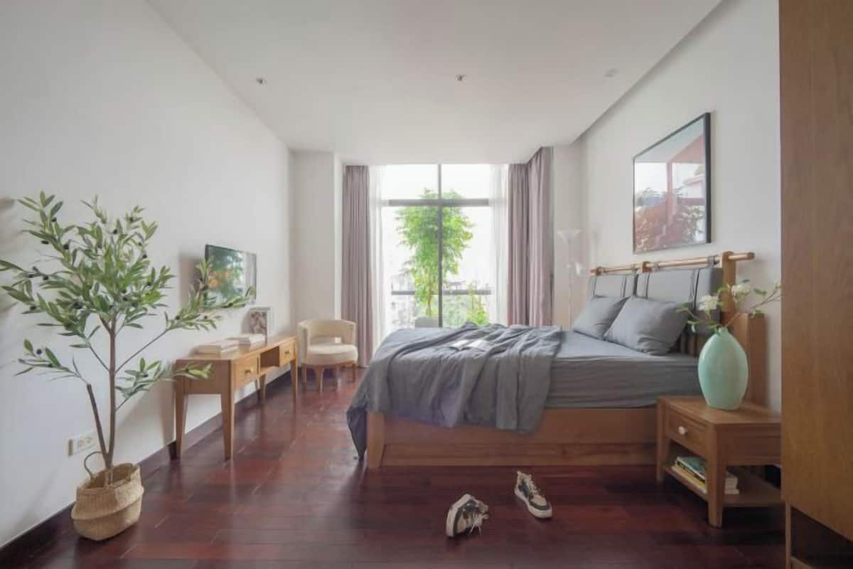 A bedroom with a bed, bedside table, chair, and a potted plant.