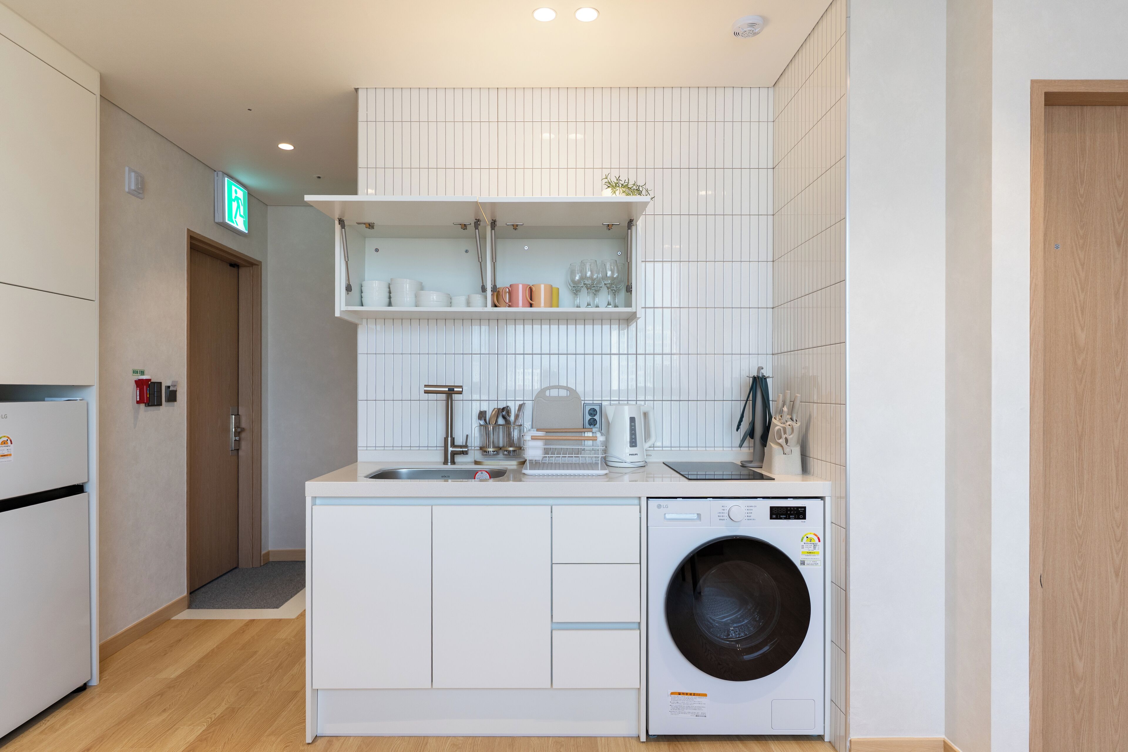 Una cocina compacta con lavadora integrada, un lavabo y un estante sobre la encimera.