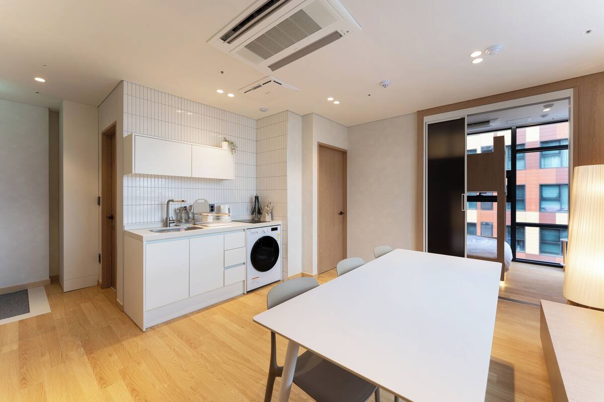 Una cocina moderna con lavadora integrada, un comedor con mesa y sillas, y vistas a la ciudad a través de amplias ventanas.
