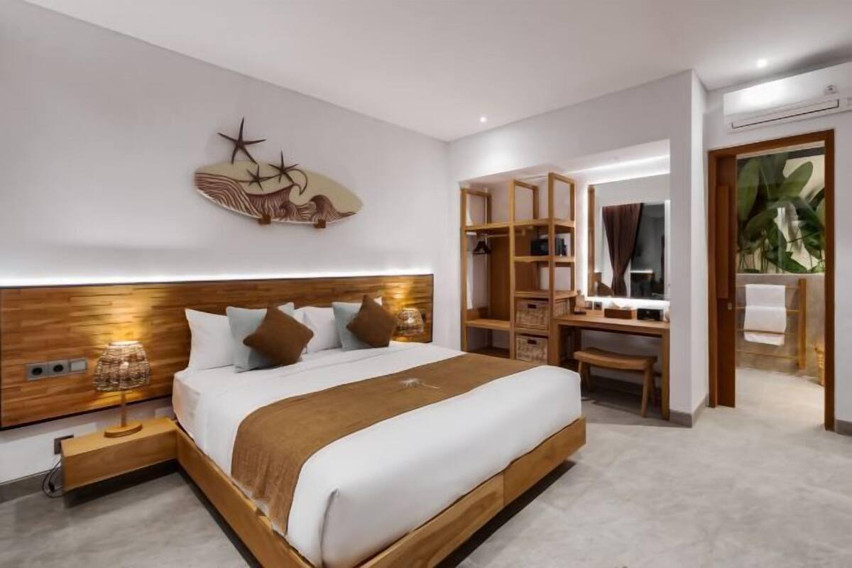 Et moderne hotelværelse med en stor seng, et træhovedgærde, sengeborde med lamper, et skrivebord og et sminkebord med spejl.
