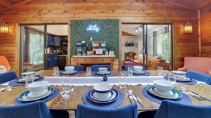 A dining area with a long table set for six, a kitchen in the background, and a neon sign above the counter. - Gloria's Hot Tub Game Room Fire Pit (Blakeslee)
