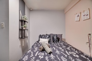 Une chambre à coucher avec un lit, une étagère fixée au mur ornée de plantes et un coussin avec un motif textuel.