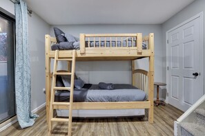 Un lit superposé avec une échelle, une petite table et une porte, dans une pièce dont le sol est recouvert de planches de bois.