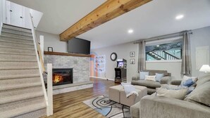 A modern living room with a fireplace, a staircase, a sofa set, and a large window with a view of a staircase. - Gloria's Hot Tub Game Room Fire Pit (Blakeslee)