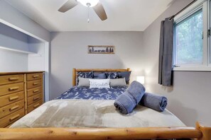 Ein Schlafzimmer mit einem hölzernen Bett, einem Deckenventilator, einem Fenster mit Vorhängen, einem Schminktisch und einer Wandleuchte.