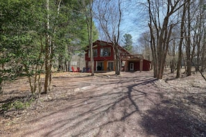 Un chalet rustique avec une allée en terre, entouré d’arbres.