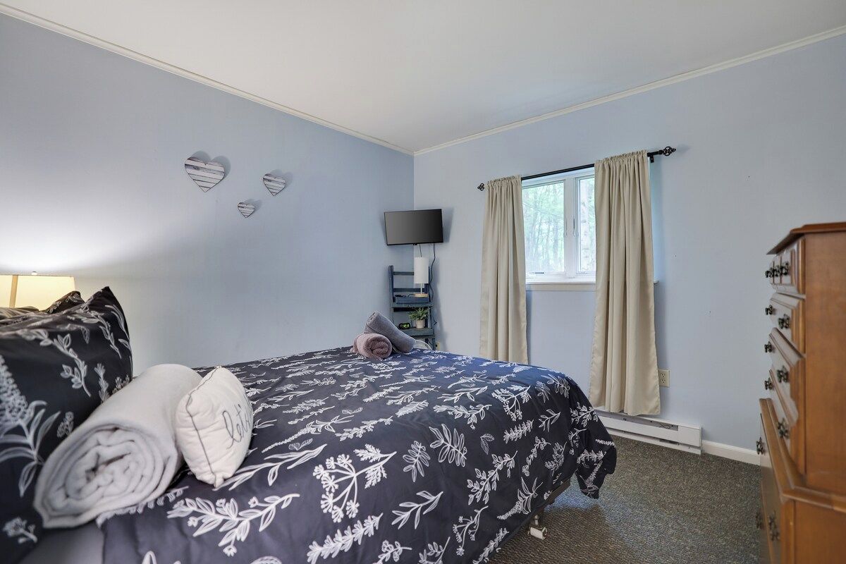 A bedroom with a bed, a dresser, a TV, and a window with curtains.