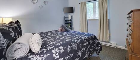 A bedroom with a bed, a dresser, a TV, and a window with curtains.