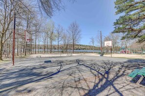 Un terrain de basket en plein air avec un banc, des arbres et une aire de jeux en arrière-plan.