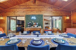 Un espace repas doté d’un plafond en bois, d’une enseigne au néon et d’une cuisine visible à travers des portes vitrées.