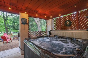 Een hoekje met een bubbelbad, een houten plafond, uitzicht op bomen en een lattenwand met een krans.