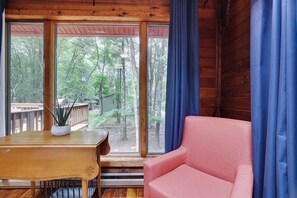 Une pièce avec une table en bois, un canapé rose et une grande fenêtre donnant sur une forêt.