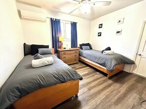 Une chambre avec deux lits simples, une commode en bois, une table de chevet et un ventilateur de plafond.