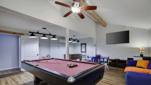 A pool table in a room with a ceiling fan, a TV mounted on the wall, and a blue sofa. - Gloria's Hot Tub Game Room Fire Pit (Blakeslee)
