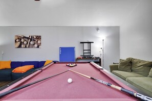 Ein Billardtisch in einem Raum mit einem blauen und einem grünen Sofa.