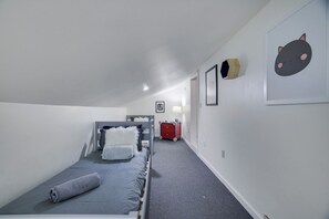 Een kleine kamer met een enkel bed, een grijs tapijt, een rode koffer en een lijstje aan de muur.