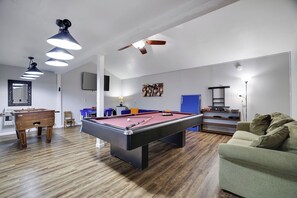 Ein Billardtisch in einem Raum mit Deckenventilator, einer Couch und Holzboden.