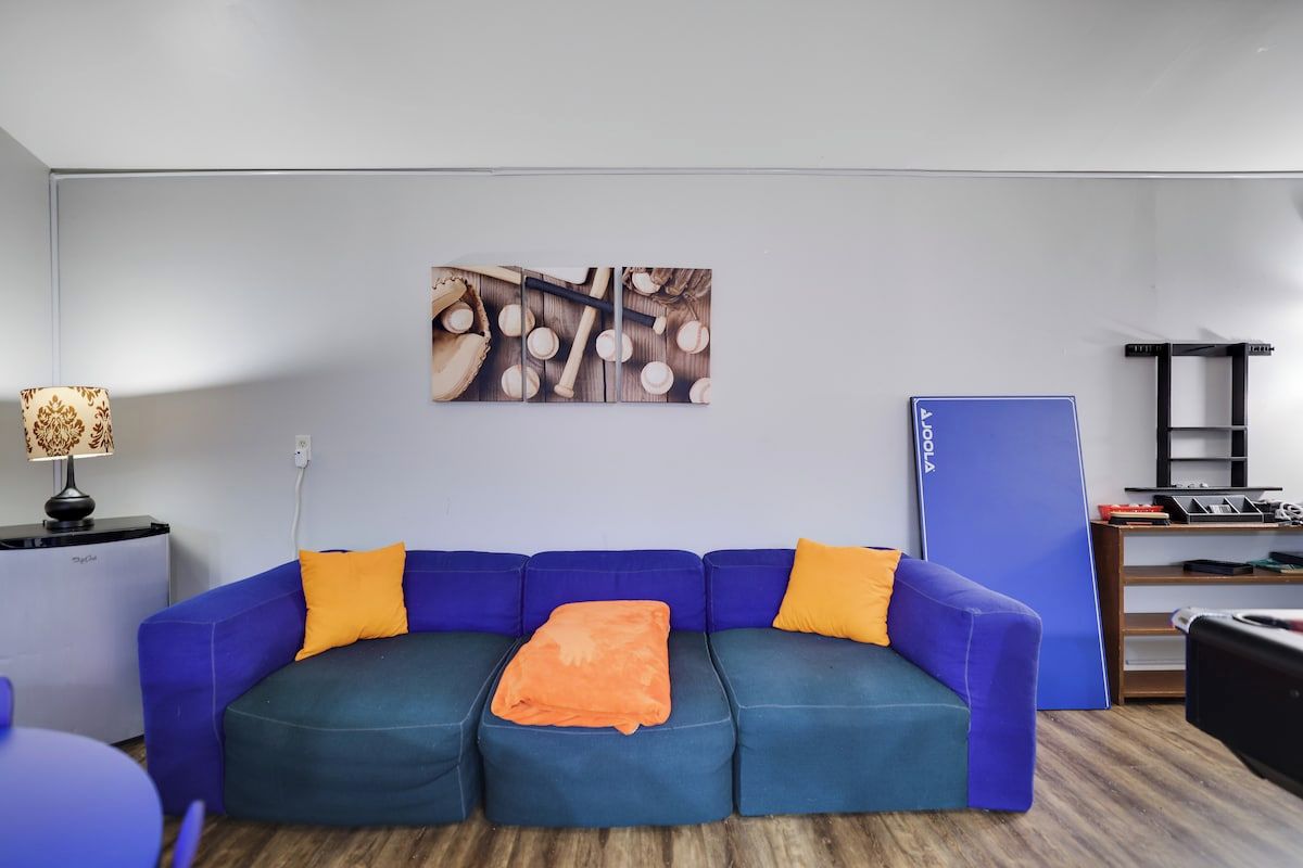 A modern living room with a blue sofa, orange cushions, a wooden floor, a wall-mounted artwork, and a blue cabinet.