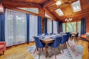 Une salle à manger avec une table en bois dressée pour six personnes, entourée de chaises bleues, dans une cabane aux murs en bois et au plafond en pente.