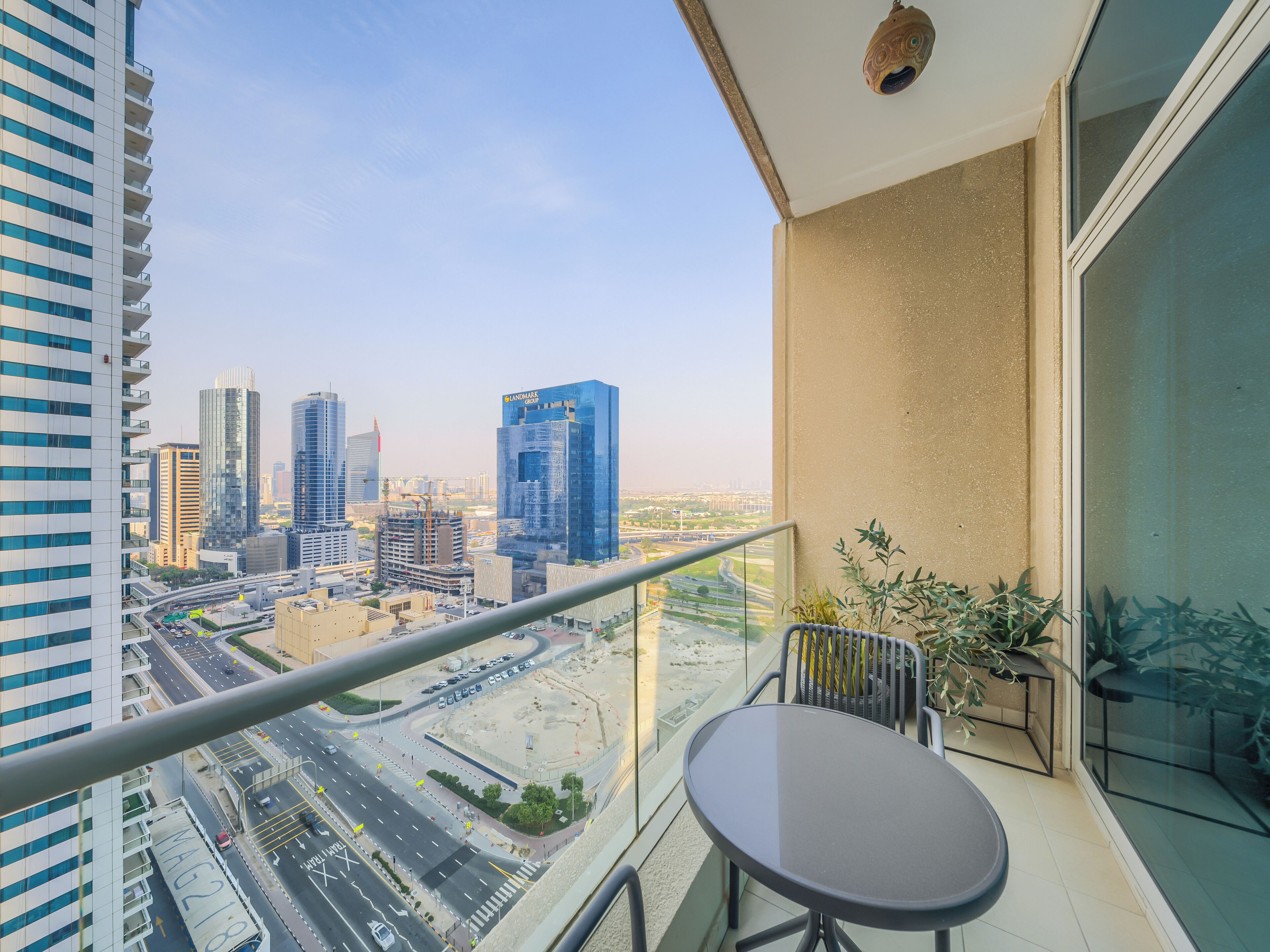 A balcony with a table and chairs, overlooking a cityscape with modern buildings and a highway.