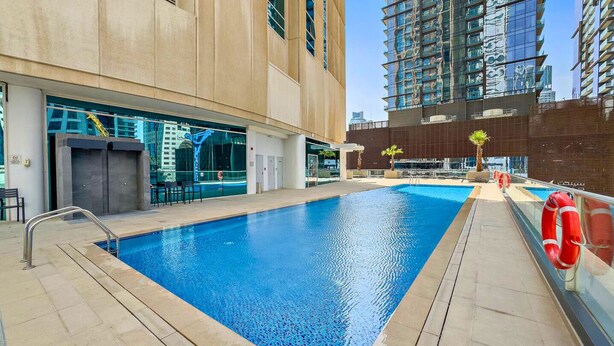 Piscina com design moderno, cercada por um edifício com grandes janelas e vista para outros arranha-céus.