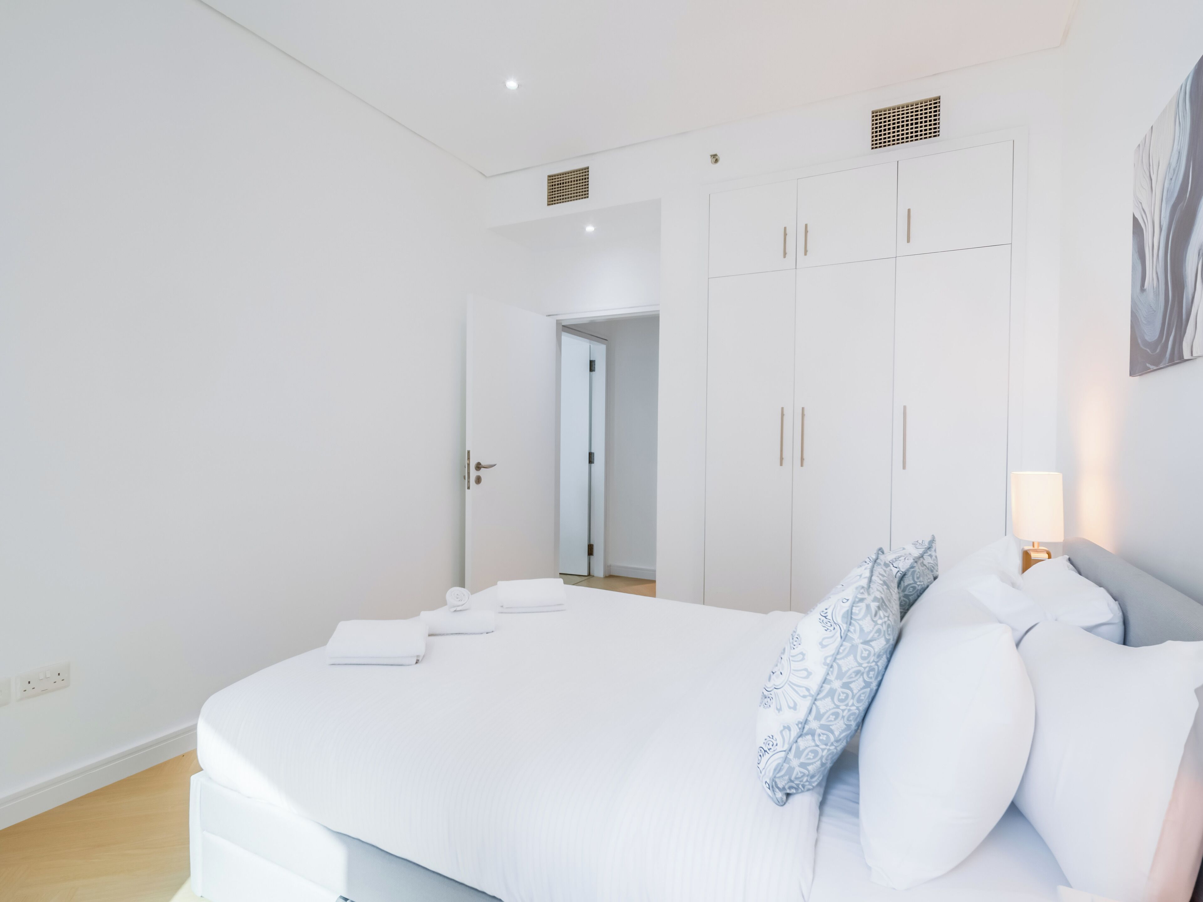 A modern bedroom with a large bed, white walls, and a wardrobe.
