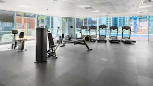 Uma academia com diversos equipamentos de exercício, amplas janelas e vista para o horizonte urbano.